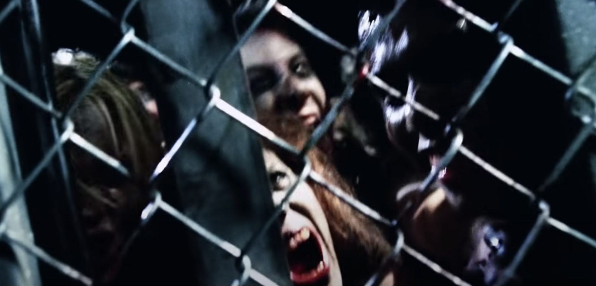 A bunch of blood-thirsty zombies snarl from behind a chain link fence