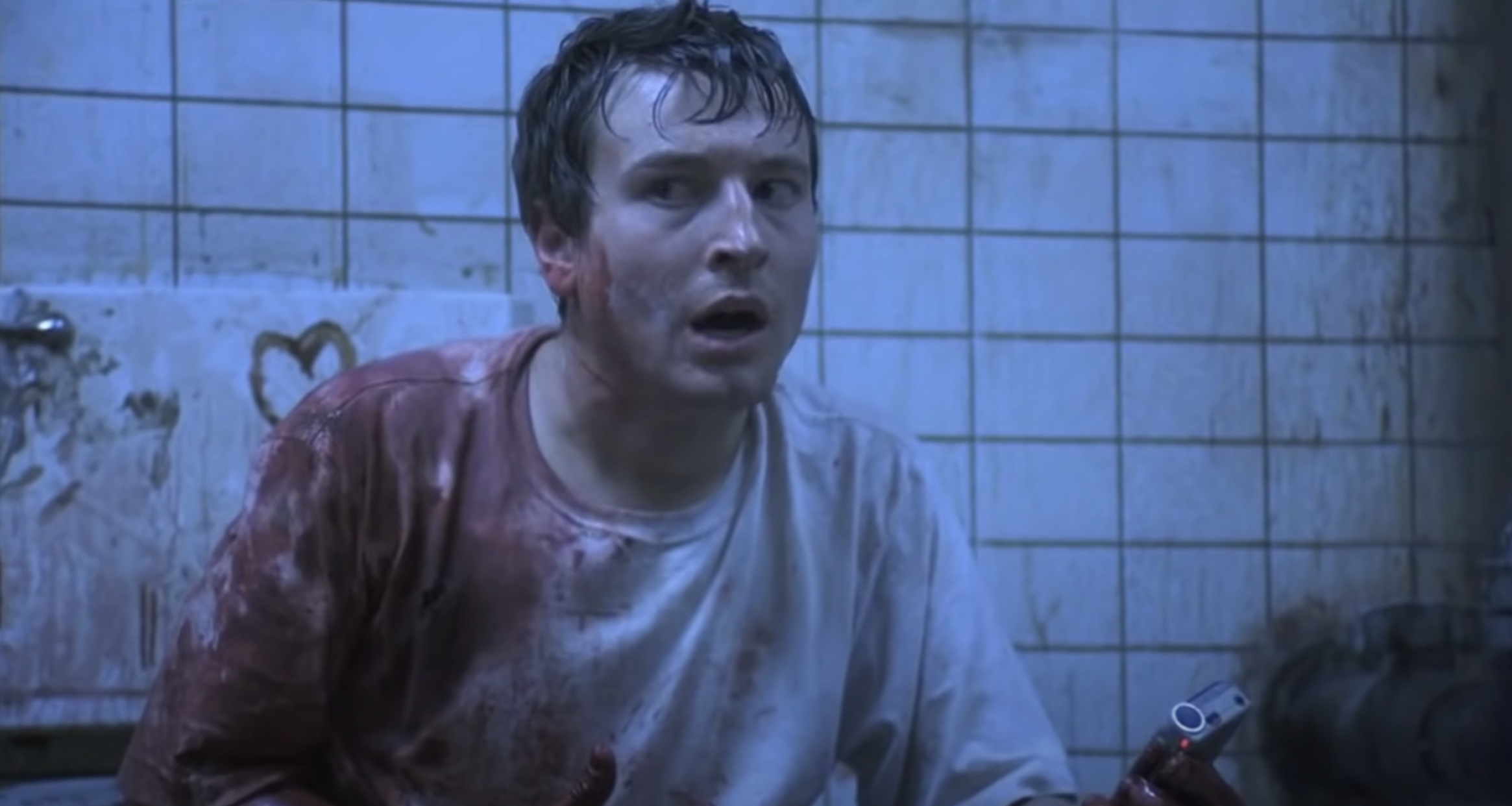 A man covered in blood looks scared and concerned while holding a tape recorder