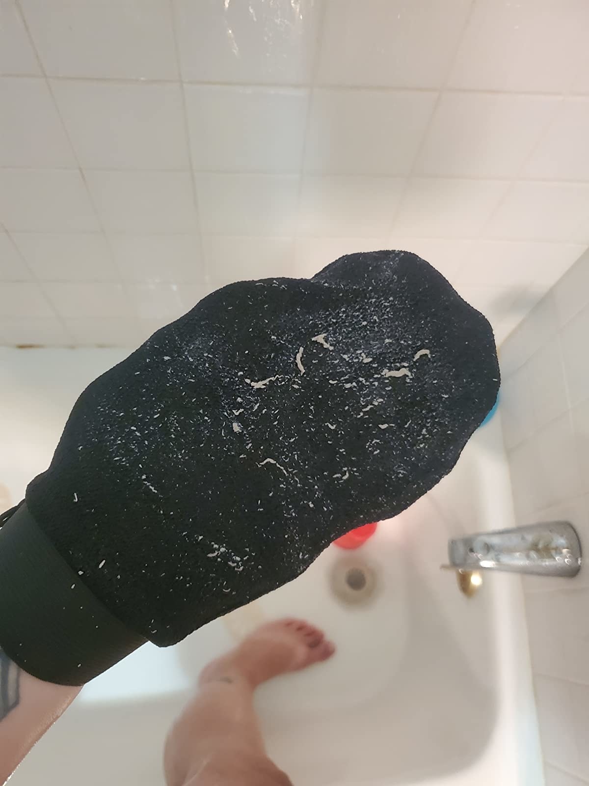 reviewer holds black exfoliating mitt covered in dead skin while taking a shower