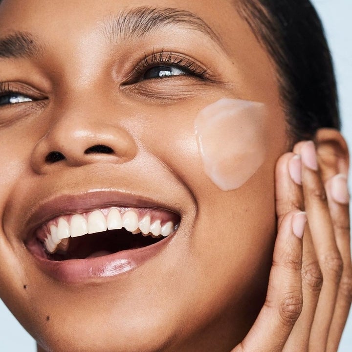 a smiling person applying the cream to their cheek