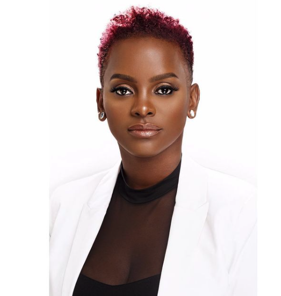 A headshot of a Black woman with short pink hair 