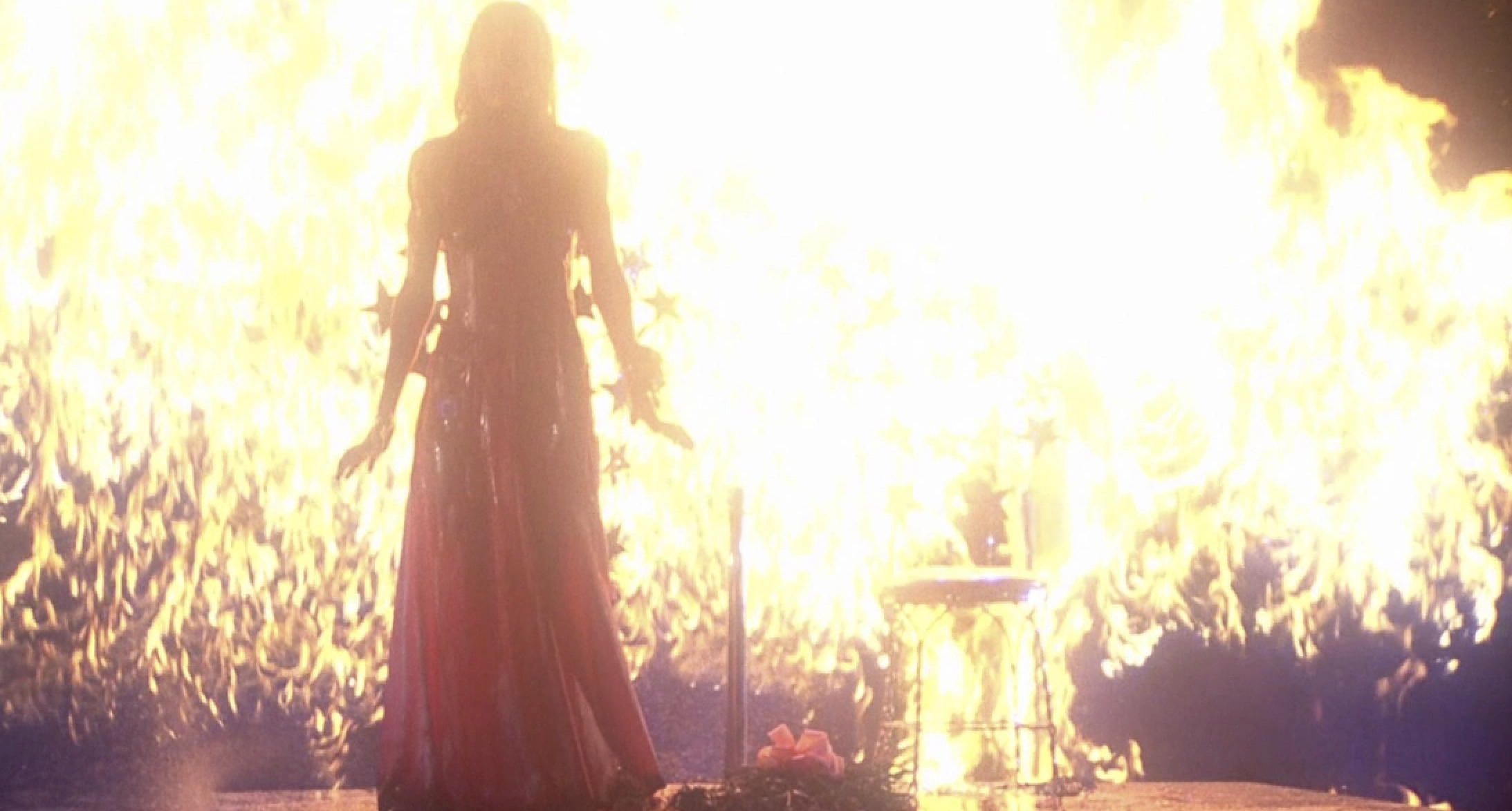 Carrie stands onstage covered in blood as everything around her is engulfed in flames