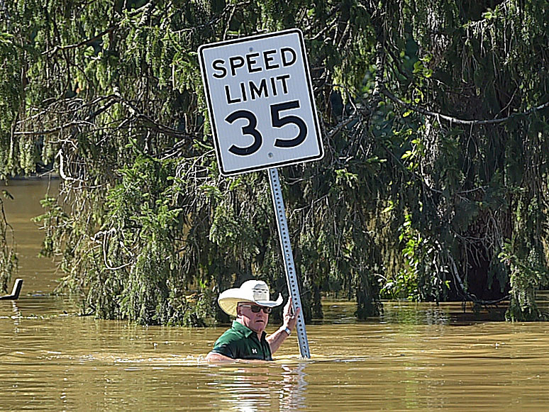 A man wearing a wide-brimmed hat walks in water up to his mid-chest while holding a &quot;Speed limit 35&quot; sign