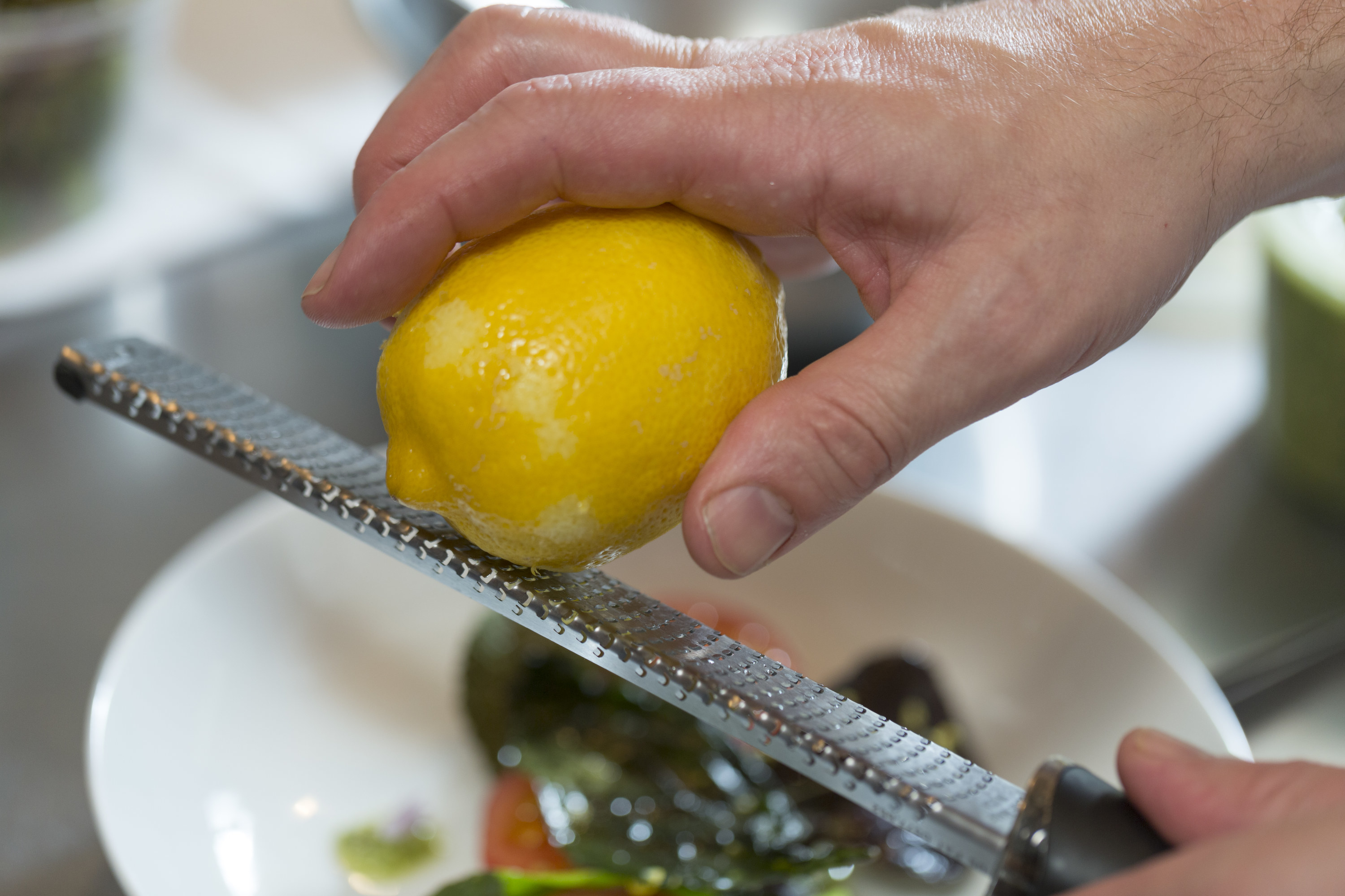 Zesting a lemon on a microplane over a bowl of food