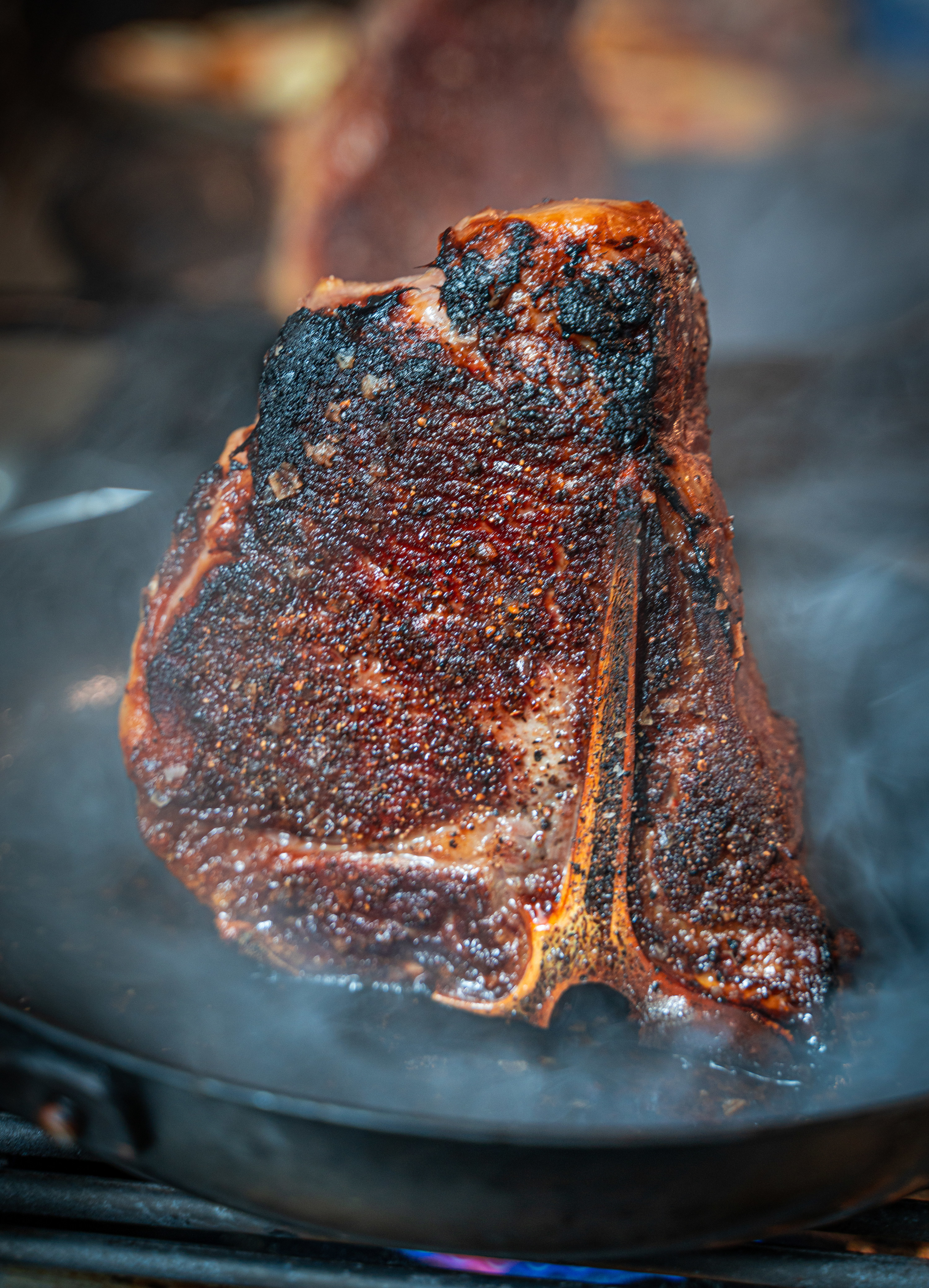 Darkly seared steak in a cast iron skillet with pieces of freshly cracked black pepper on it