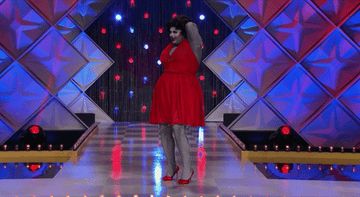 drag queen on the runway painted grey, taking off a red dress to reveal red lingerie