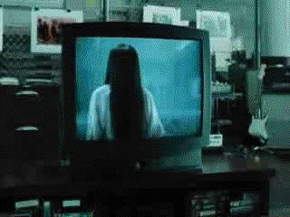 A figure with black hair covering her face crawls out of the TV and walks through the living room