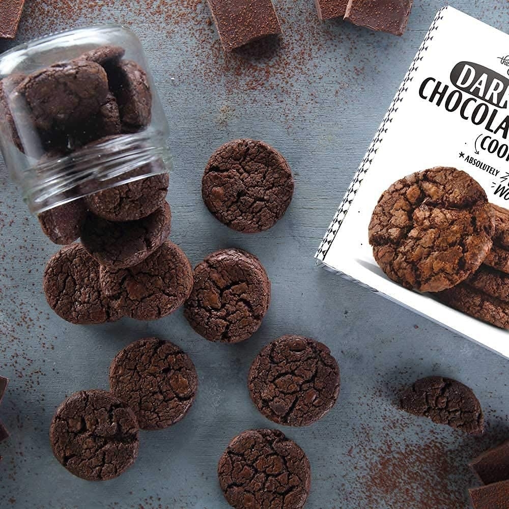 Dark chocolate cookies in a box next to cookies on a table