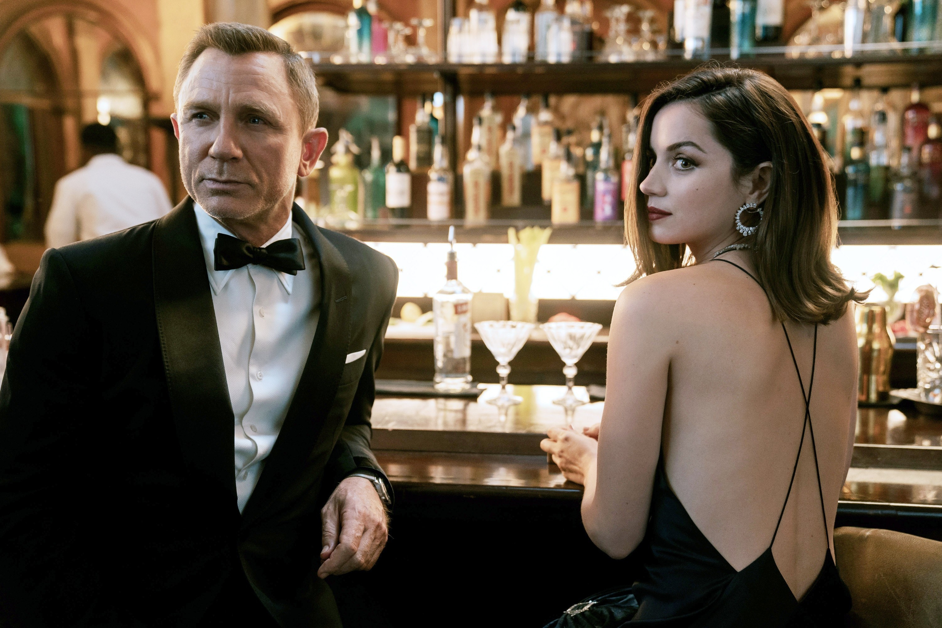 Daniel a Bond in a tuxedo standing at the bar with Ana de Armas as Paloma wearing a backless outfit in No Time to Die