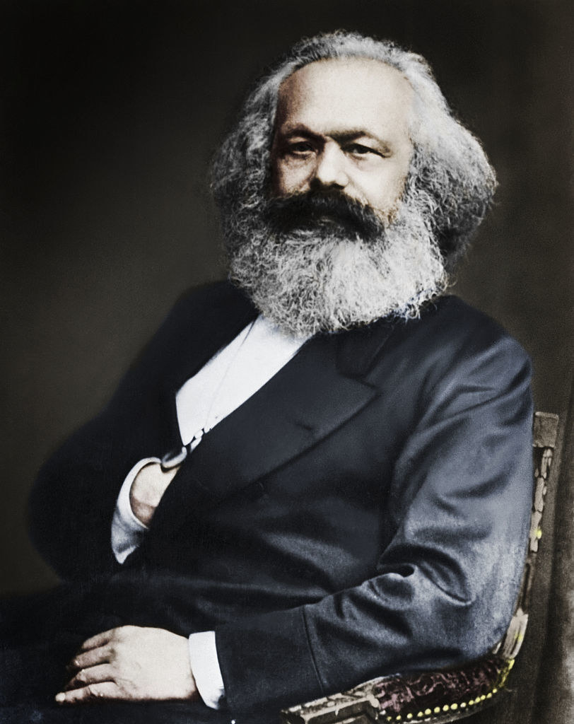 Karl Marx with a major beard sitting in a chair