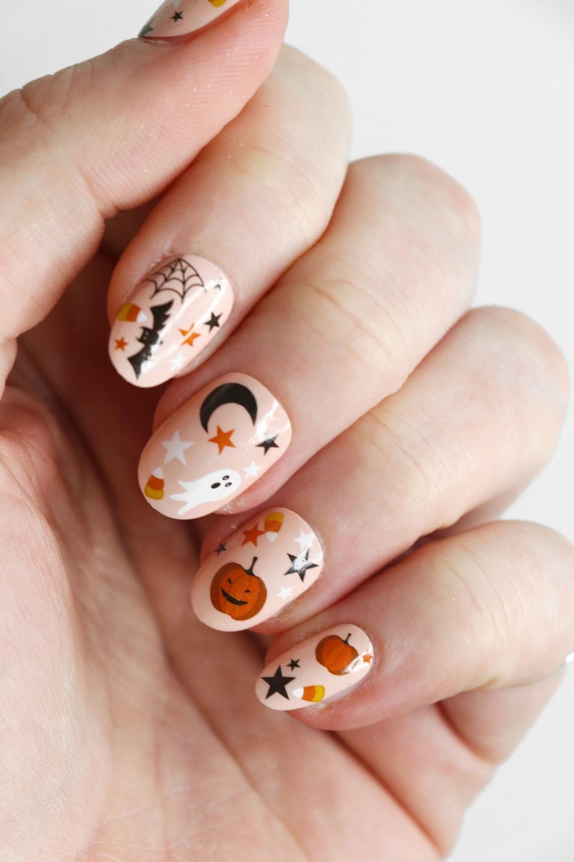 A person&#x27;s hand with short painted fingernails that have little pumpkins stars and ghosts on them