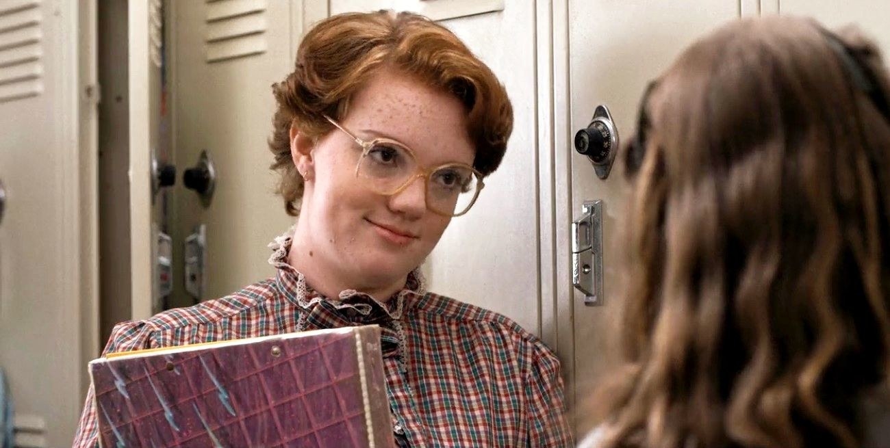 Shanon Purser as Barb in &quot;Stranger Things&quot; leaning against the school locker while holding a binder.