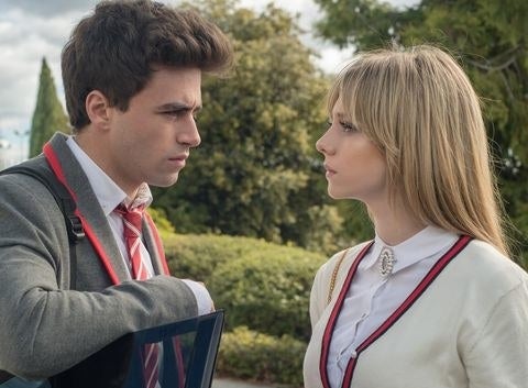 Ester and Itzan as Carla and Samuel from &quot;Elite&quot; in school uniforms looking at each other, with Itzan&#x27;s hand resting on the car door.