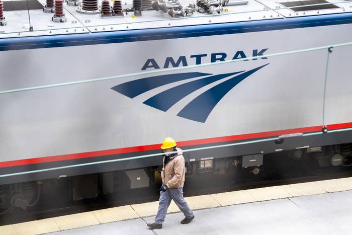 Person wearing a hard hat walks along a platform by an Amtrak train