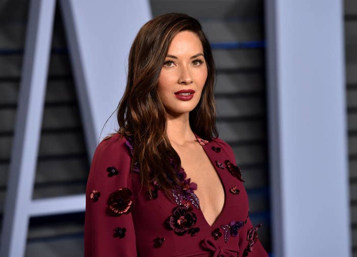 Olivia looks off camera on the red carpet, she&#x27;s wearing a plunging maroon dress adorned with 3D flowers