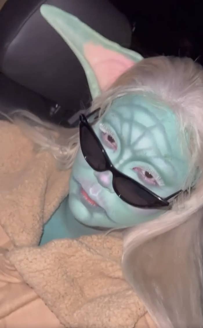 Lizzo wearing full face paint and prosthetic ears to resemble Baby Yoda, along with a pair of pointed, glamorous sunglasses