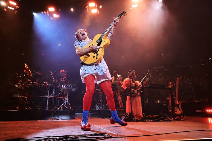 Harry onstage playing a guitar in his Dorothy costume