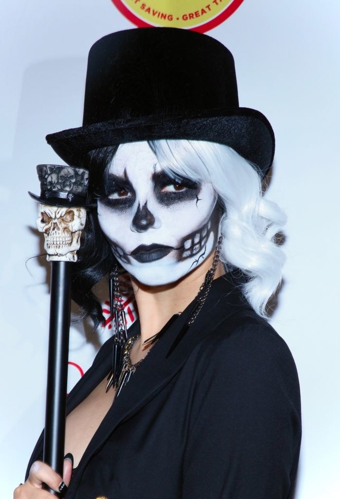 Victoria in a top hat, suit jacket, and skull face paint, with a cane topped by a skull