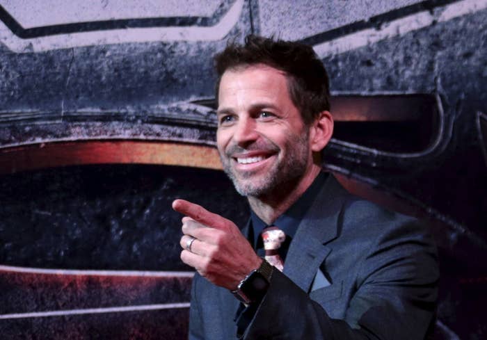 Zack Snyder standing behind a poster for "Batman v Superman: Dawn of Justice"