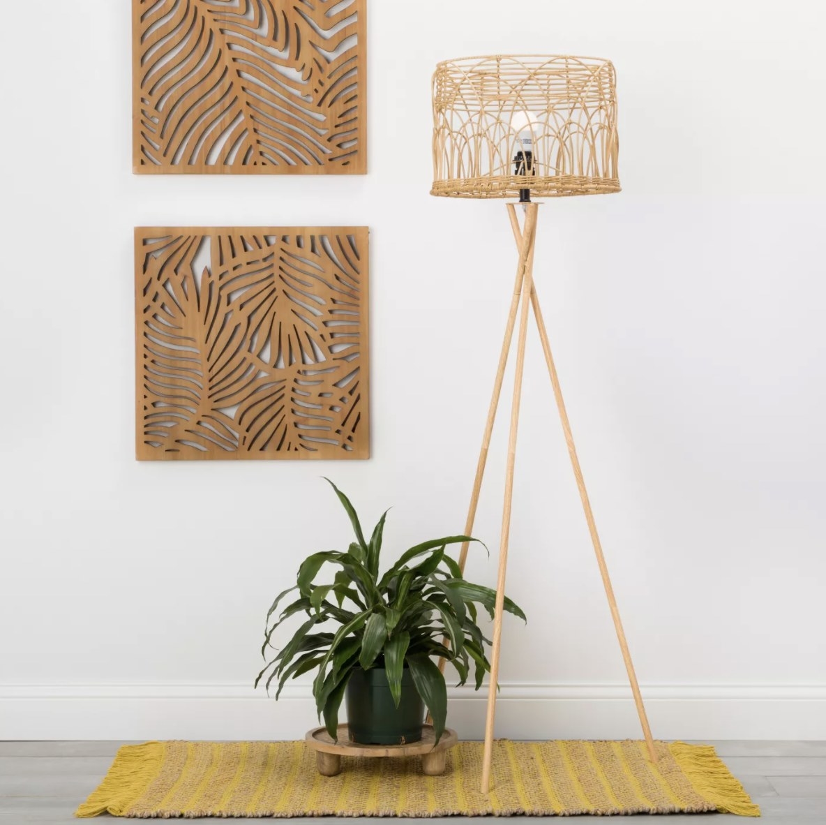 There are two wooden square palm leaf panels are hung on a blank wall and are surrounded by boho decor