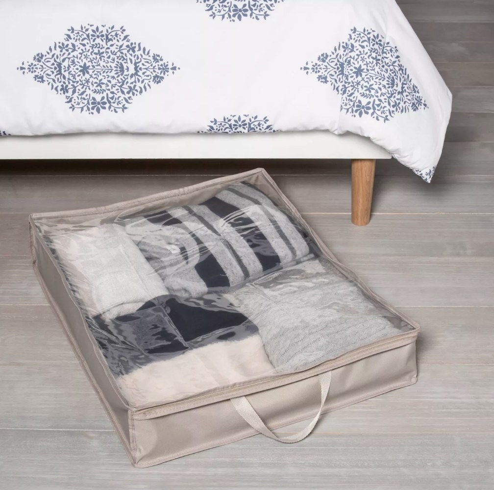 A gray/plastic under the bed storage bag filled with clothes