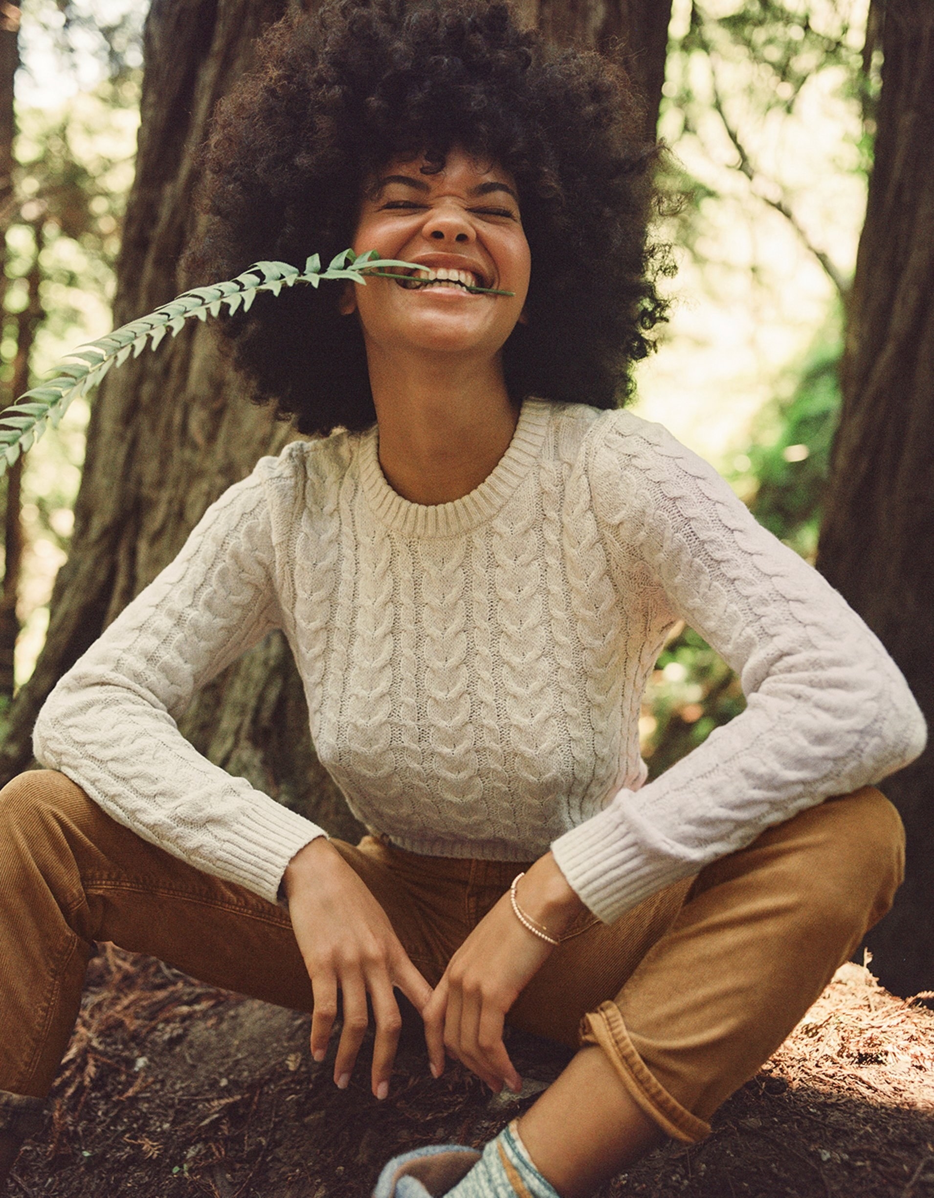 model wearing the form fitting knit sweater in a forest with brown pants and boots
