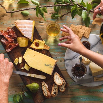 two hands in front of several types of cheeses on a board
