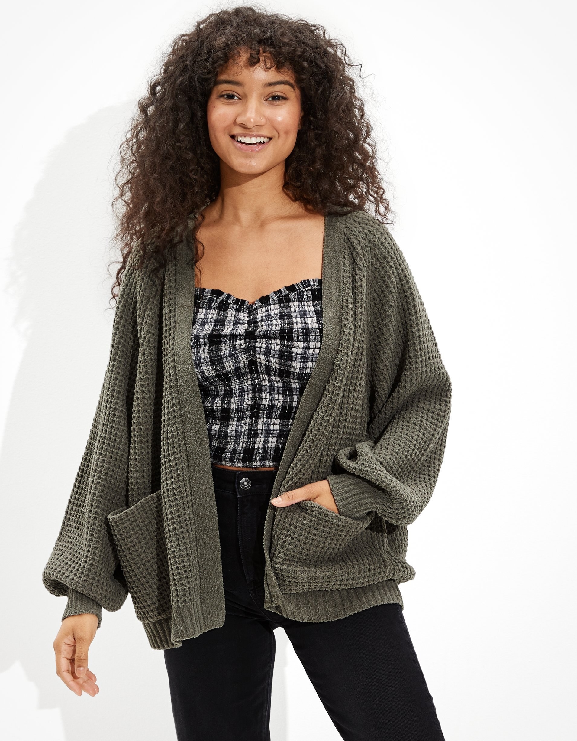Model wearing chunky cardigan. it has no buttons, includes front pockets, and sleeves that are fitted at the wrist.