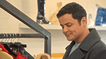 A gif of a person rubbing a sleeve of a yellow sweater across their cheek and smiling