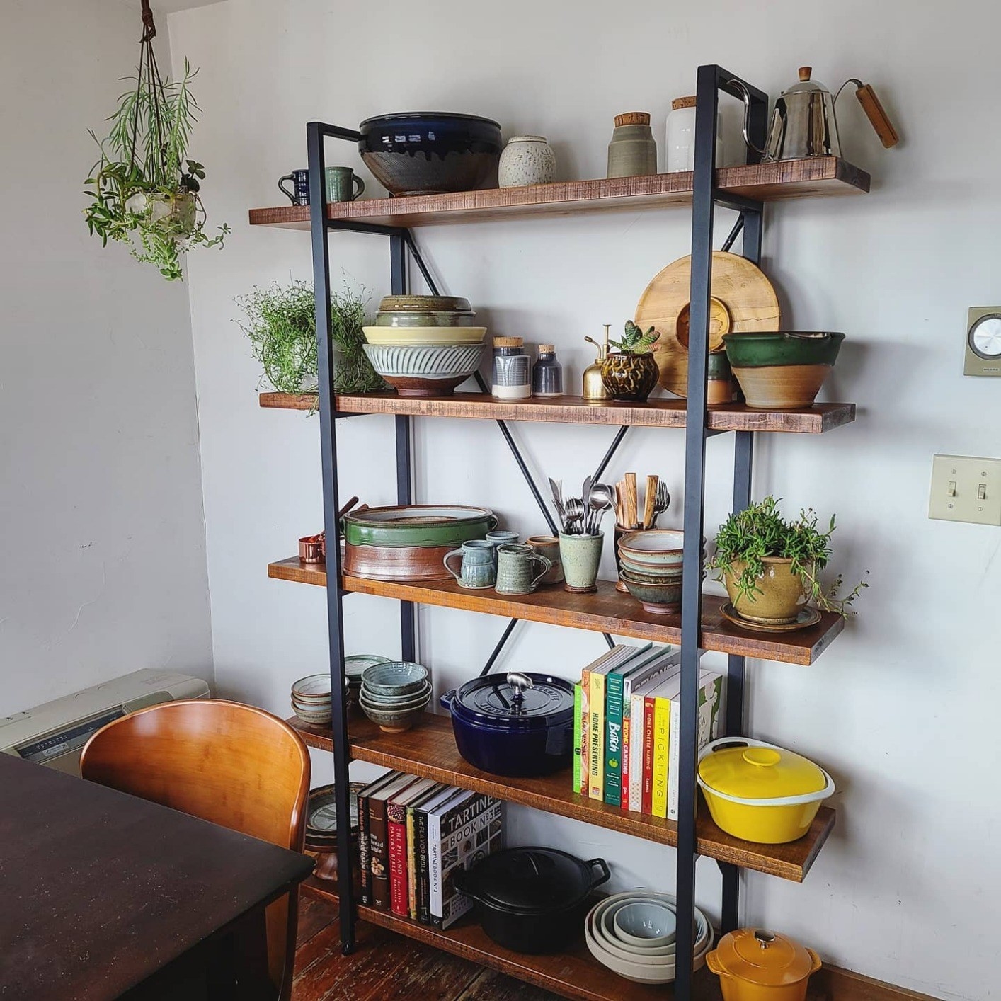 five-tier wood shelf with black metal frame holding reviewer&#x27;s cookware, books, and plants
