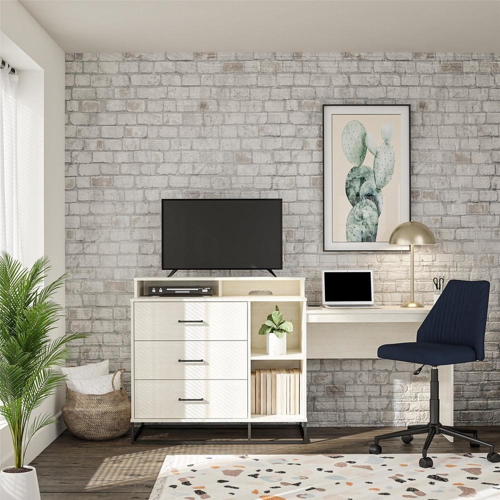 off-white dresser with three textured drawer, shelves, a TV on top, and a desk on the side