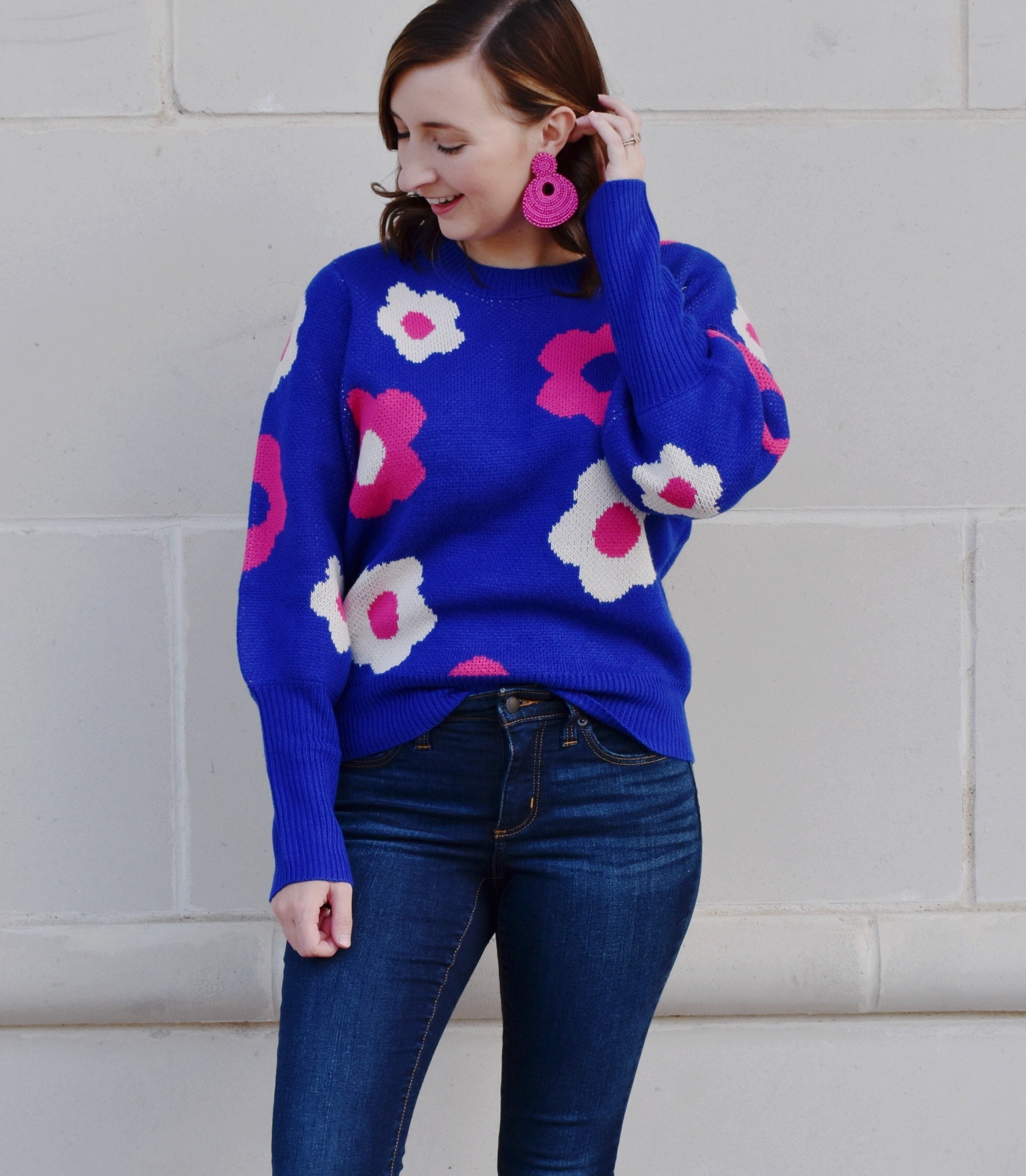 Model is wearing a bold blue sweater with pink and white retro flowers printed on it