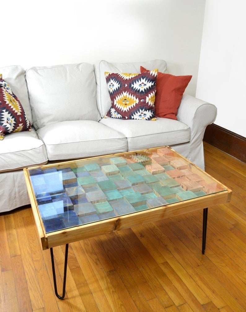 wood coffee table with metal legs and glass top, under the glass are squares of wood in different heights and a gradient of greens and blues