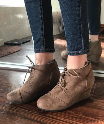 a reviewer wearing skinny jeans and the lace-up wedge booties in brown suede