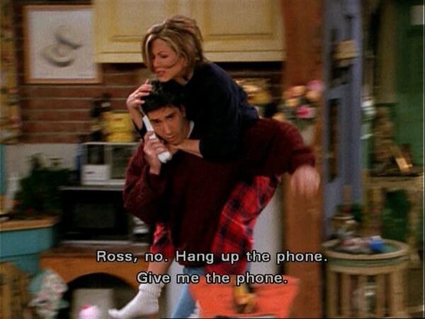 Ross listening to a message from Rachel as she jumps on his back and tries to stop him