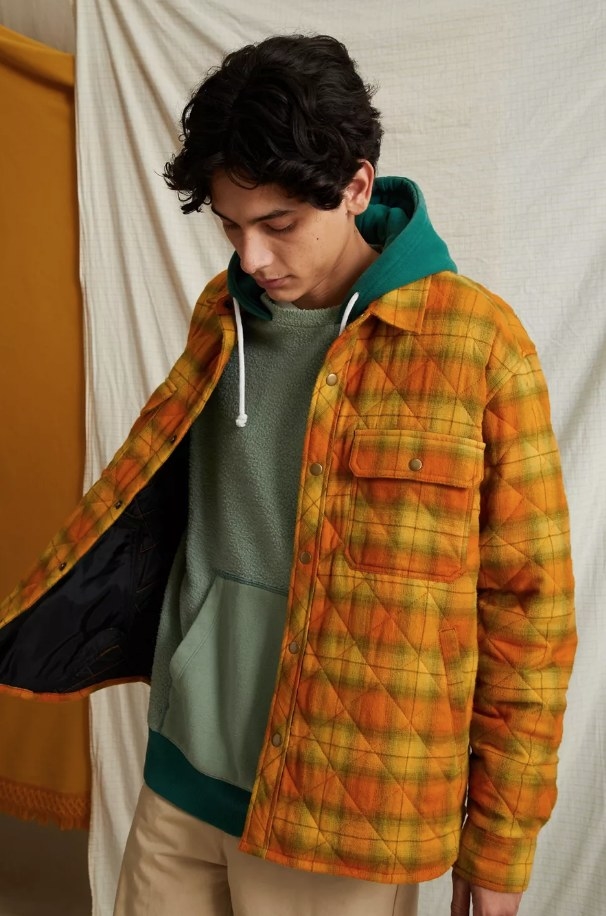 Model wearing quilted orange, green and yellow plaid jacket over green shirt