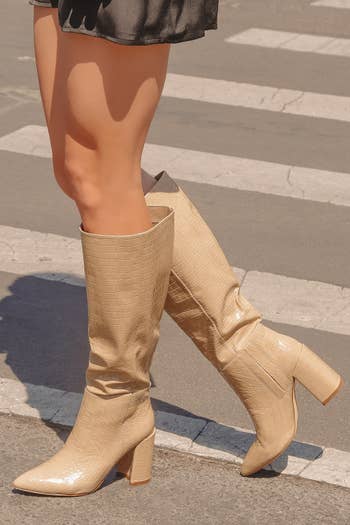 a model wearing a mini skirt and the knee-high boots in tan