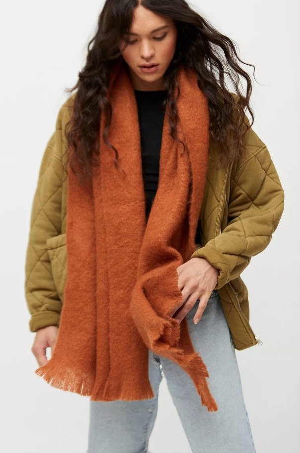Model wearing orange scarf with tan jacket