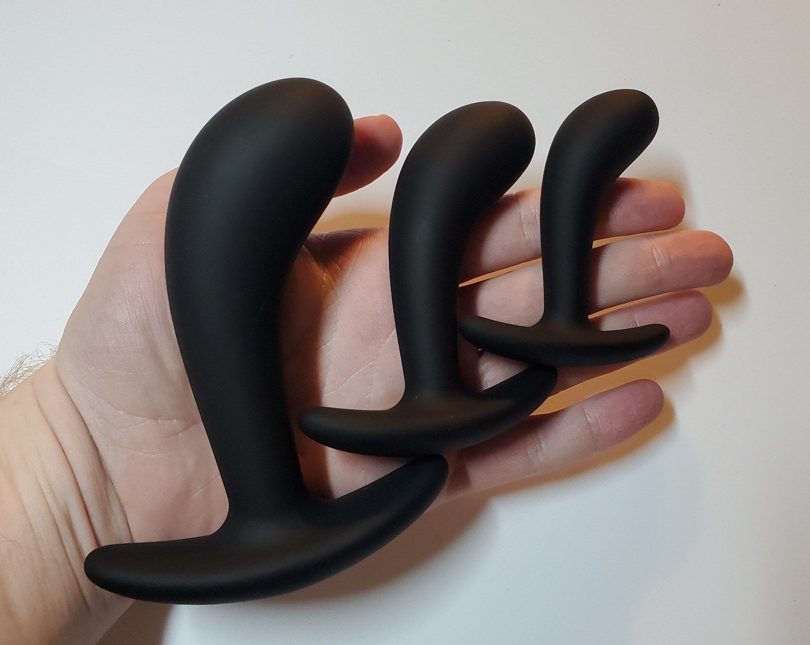 A reviewer holding the small, medium, and large plugs, each with a flared base and curved shaft