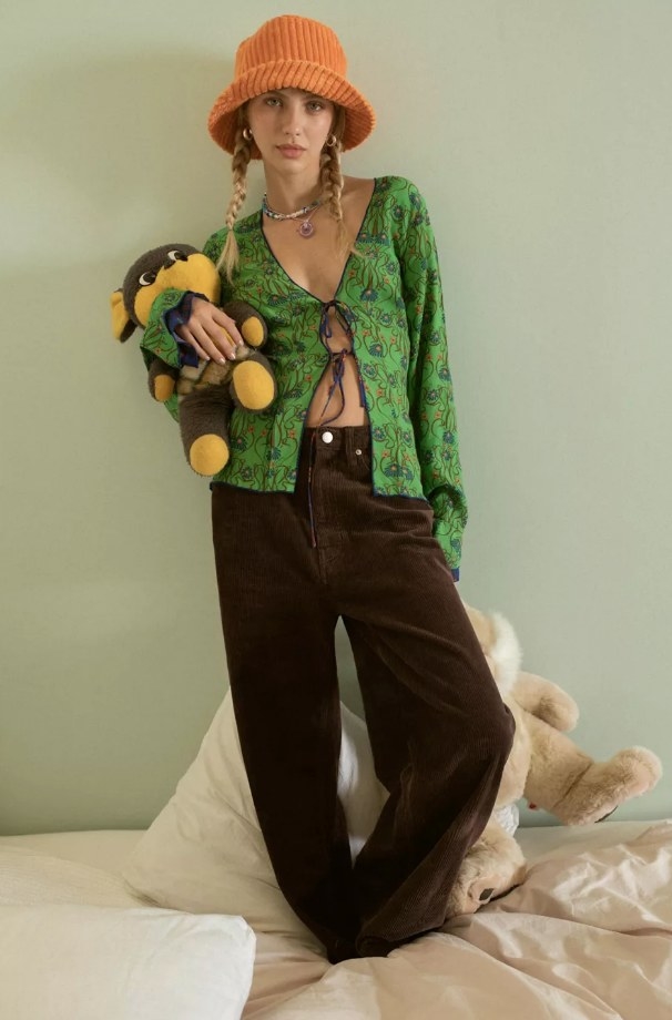 Model wearing brown corduroy pants with green shirt and orange hat