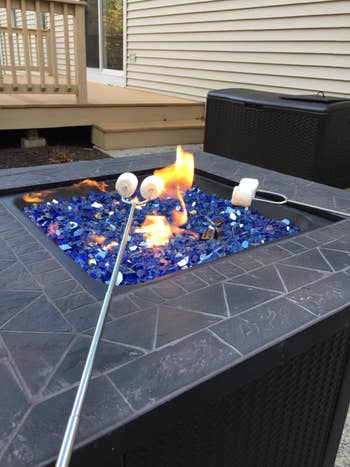 Reviewer using the stick to roast marshmallows over a fire pit