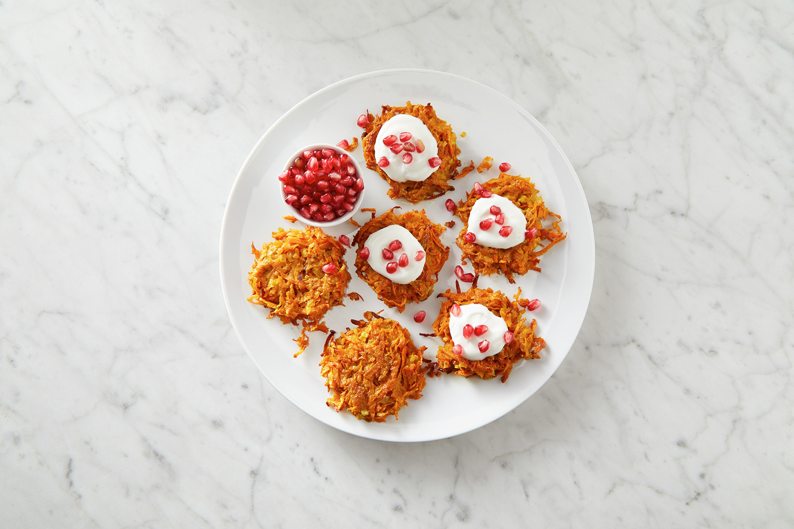 A plate of latkes garnished with sour cream and pomegranate seeds.