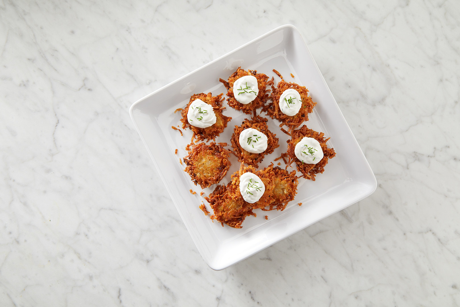 A plate of latkes with dollops of sour cream garnished with chives.