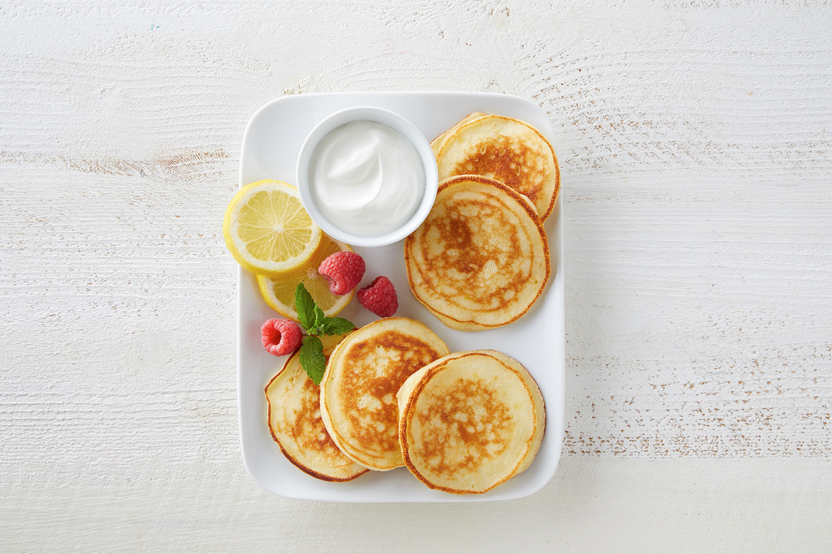 A plate of pancake-like cheese blintzes with strawberries, lemon slices, and sour cream.