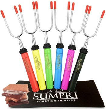 Six roasting sticks with colorful handles next to s'mores