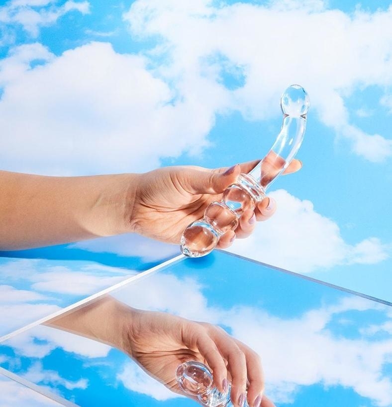 Model holding double-ended glass dildo above mirror