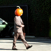person in a business suit walking with a jack-o&#x27;-lantern on their head
