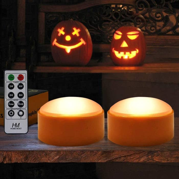 Two orange lights and a remote sitting next to two jack-o-lanterns