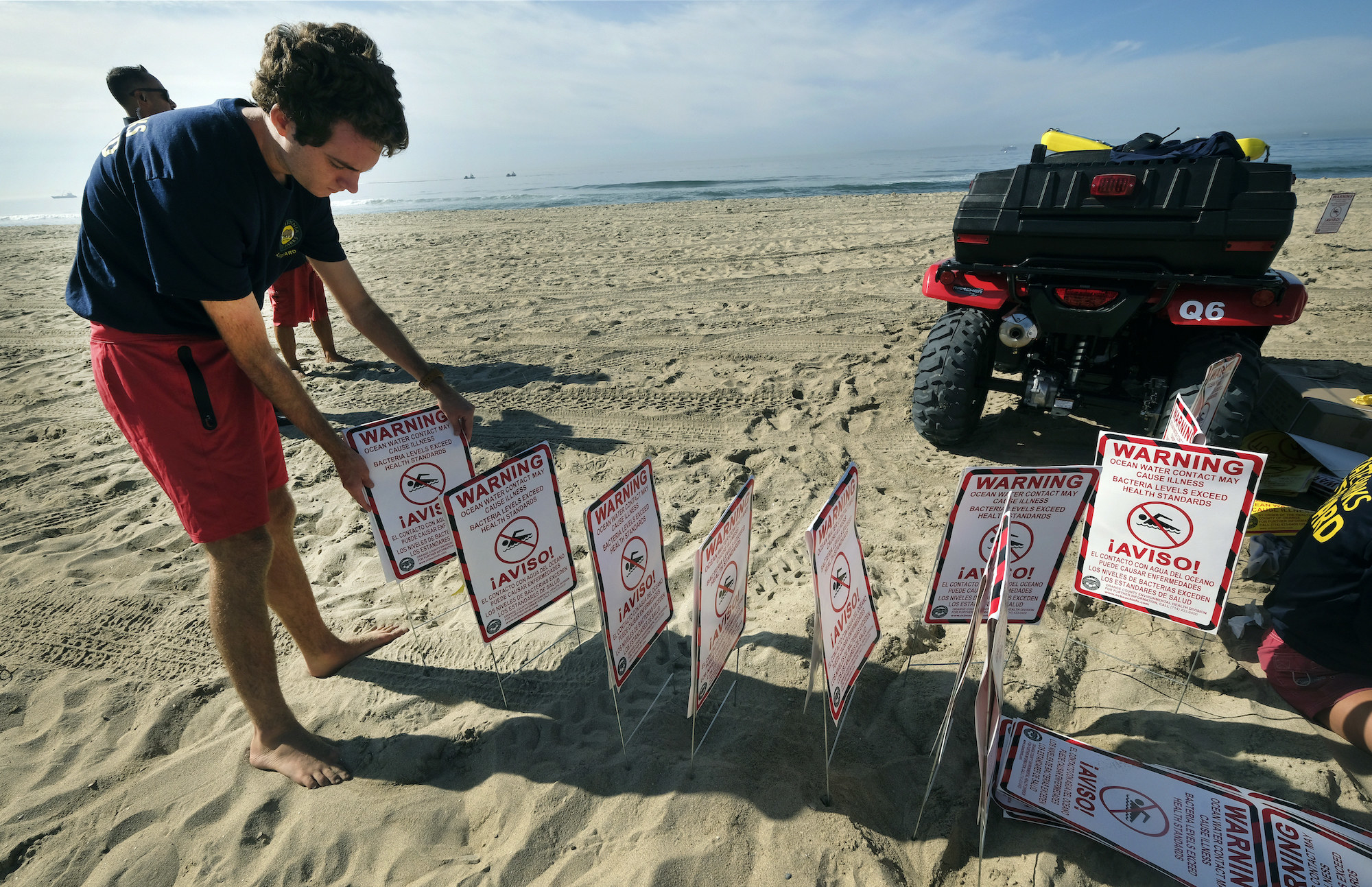 Young man arranges signs on the beach warning against swimming