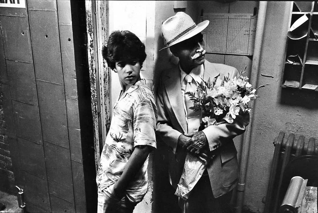A young man and an old man with flowers lean on a post at the entrance to an apartment building